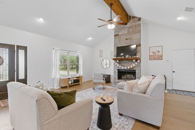 living room featuring ceiling fan, a stone fireplace, visible vents, beamed ceiling, and light wood-style flooring