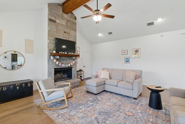 living area featuring a ceiling fan, a stone fireplace, visible vents, beam ceiling, and wood finished floors