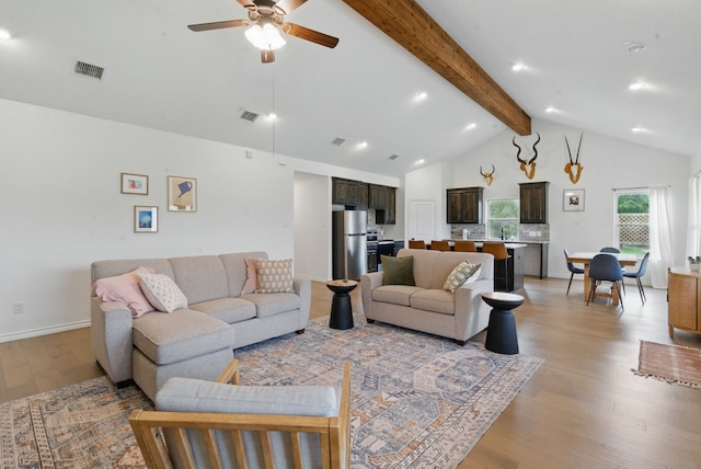 living area with visible vents, a ceiling fan, light wood-style floors, and beam ceiling