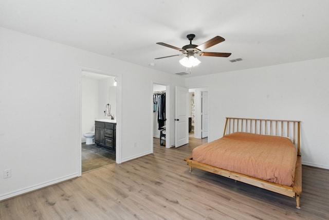 bedroom with ensuite bath, baseboards, a spacious closet, light wood-type flooring, and visible vents
