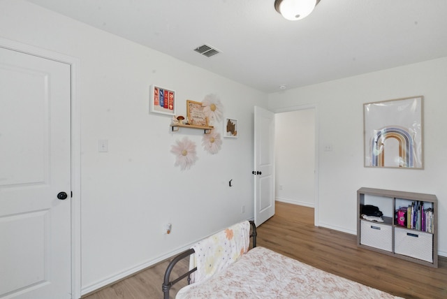 bedroom with baseboards, visible vents, and wood finished floors