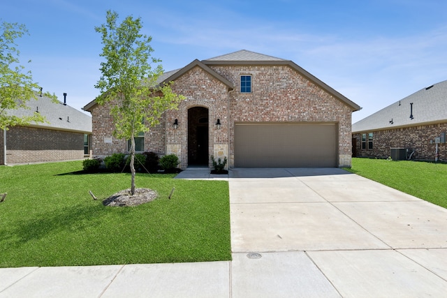 french provincial home with a garage, a front yard, brick siding, concrete driveway, and central air condition unit