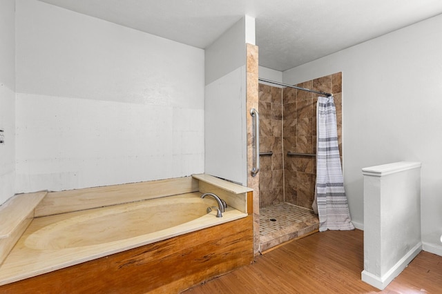 full bathroom featuring baseboards, wood finished floors, a bath, and a stall shower