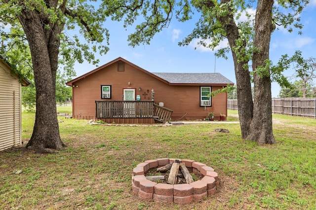 back of property featuring a lawn, a deck, fence, and an outdoor fire pit