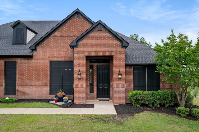 view of front of house featuring brick siding, roof with shingles, and a front lawn