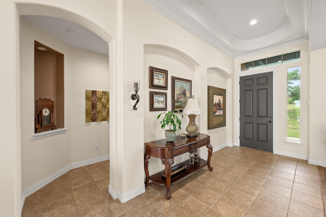 entryway featuring light tile patterned flooring, arched walkways, a raised ceiling, ornamental molding, and baseboards