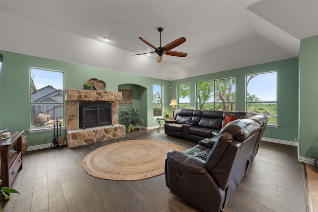 living area with a stone fireplace, plenty of natural light, baseboards, wood finished floors, and vaulted ceiling