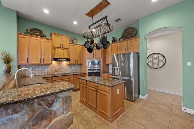 kitchen featuring appliances with stainless steel finishes, a sink, arched walkways, dark stone counters, and backsplash