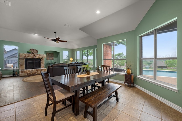 dining room featuring a stone fireplace, lofted ceiling, baseboards, ceiling fan, and light tile patterned floors