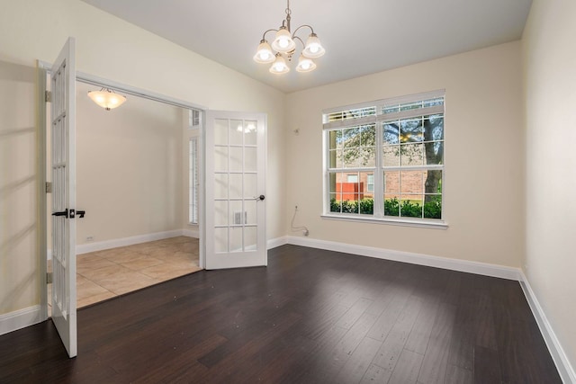 empty room with baseboards, an inviting chandelier, french doors, and wood finished floors