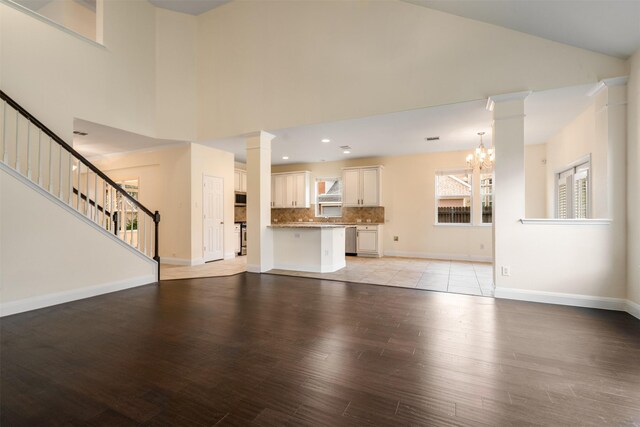 2719 Foxpoint Trl, Arlington, TX 76017 - unfurnished living room with high vaulted ceiling, light wood-style floors, a chandelier, stairway, and decorative columns