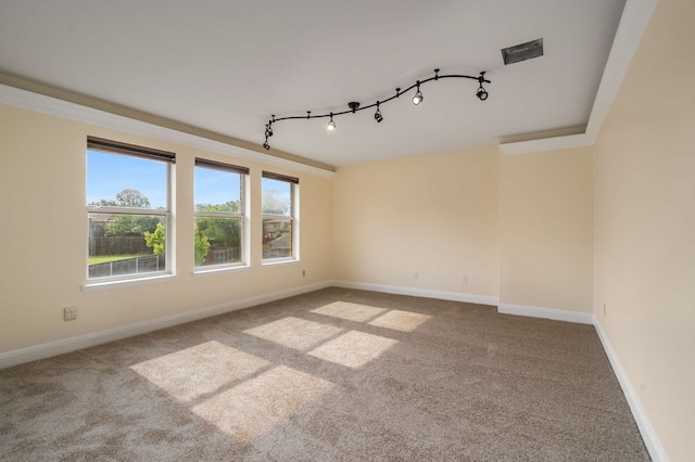 empty room with carpet floors, baseboards, track lighting, and crown molding