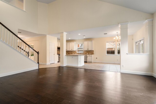 2719 Foxpoint Trl, Arlington, TX 76017 - unfurnished living room featuring light wood finished floors, high vaulted ceiling, a chandelier, stairway, and ornate columns