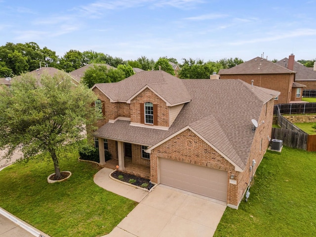 traditional home featuring a front yard, roof with shingles, a garage, brick siding, and fence