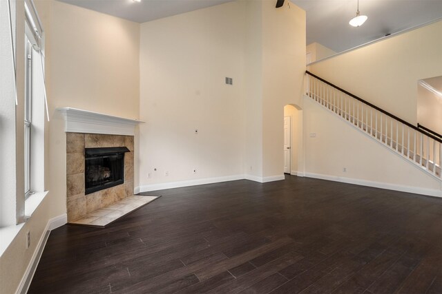 2719 Foxpoint Trl, Arlington, TX 76017 - unfurnished living room featuring wood finished floors, a tile fireplace, stairs, arched walkways, and a towering ceiling