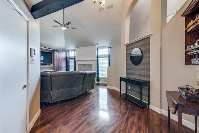 living area with wood finished floors, a ceiling fan, vaulted ceiling with beams, and a fireplace