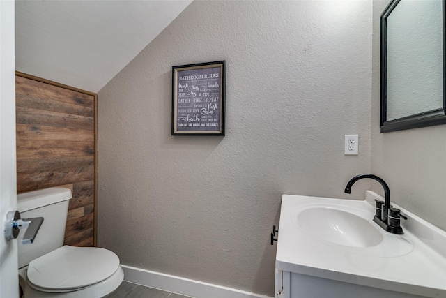 half bath with toilet, baseboards, lofted ceiling, and vanity