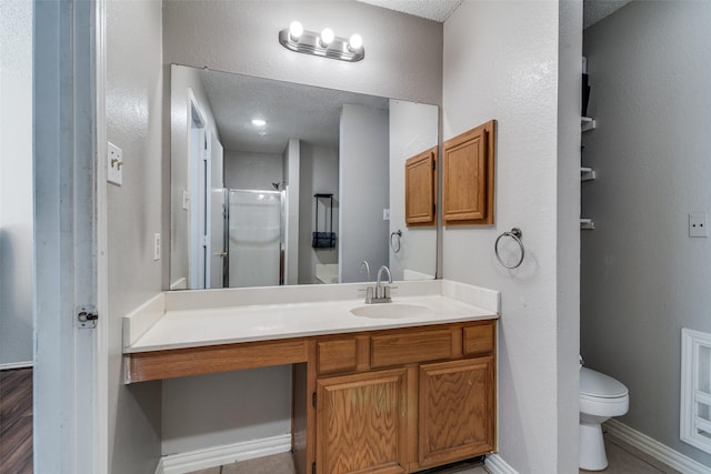 full bathroom featuring vanity, toilet, a textured ceiling, baseboards, and a shower with door