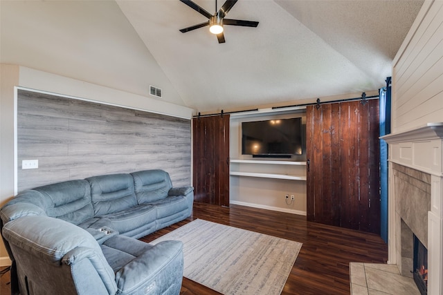 living area with a tiled fireplace, a ceiling fan, a barn door, and visible vents