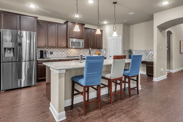 kitchen with dark brown cabinets, appliances with stainless steel finishes, tasteful backsplash, dark wood-type flooring, and a center island with sink