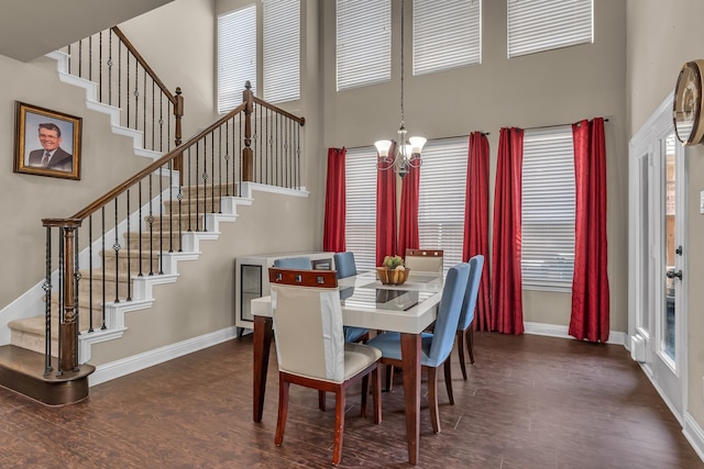 dining room with a chandelier, stairs, a wealth of natural light, a towering ceiling, and dark wood-style floors