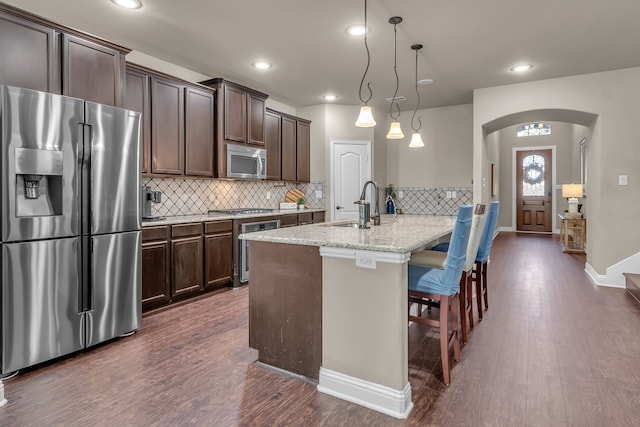 kitchen featuring a sink, appliances with stainless steel finishes, arched walkways, and dark brown cabinets