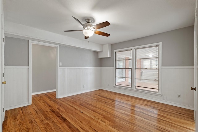 unfurnished room featuring a ceiling fan, wainscoting, and wood finished floors