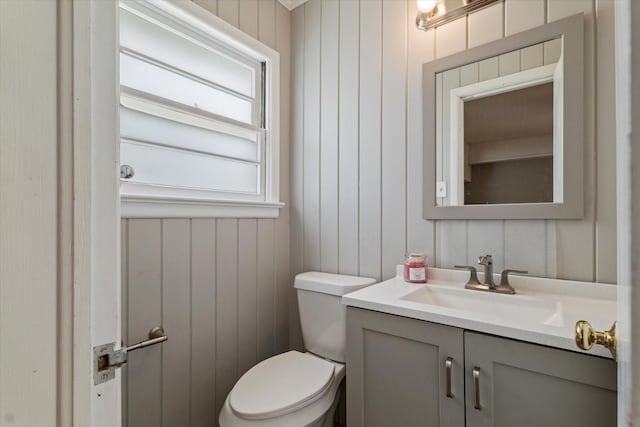 half bathroom with wooden walls, vanity, and toilet