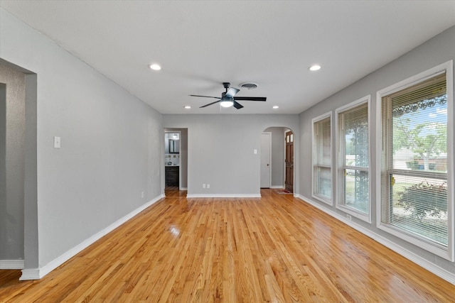 unfurnished living room featuring arched walkways, baseboards, a ceiling fan, and light wood finished floors