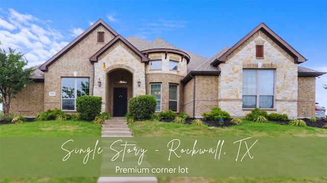french provincial home with a shingled roof, brick siding, a front lawn, and stone siding