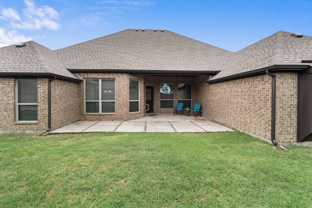 rear view of property featuring brick siding, a patio, a shingled roof, and a lawn