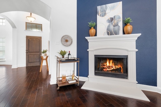 foyer featuring arched walkways, baseboards, a warm lit fireplace, and hardwood / wood-style floors