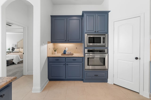 kitchen with light tile patterned floors, light stone counters, blue cabinets, appliances with stainless steel finishes, and backsplash