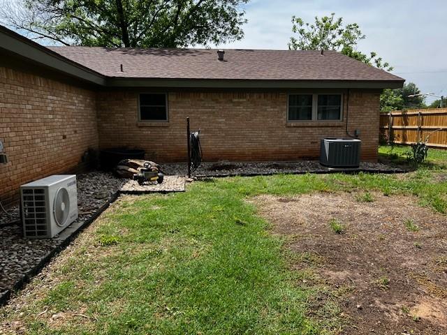 rear view of property featuring fence, roof with shingles, ac unit, brick siding, and cooling unit
