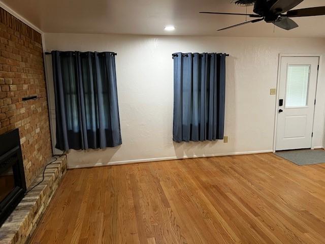 unfurnished living room with baseboards, ceiling fan, a brick fireplace, and wood finished floors