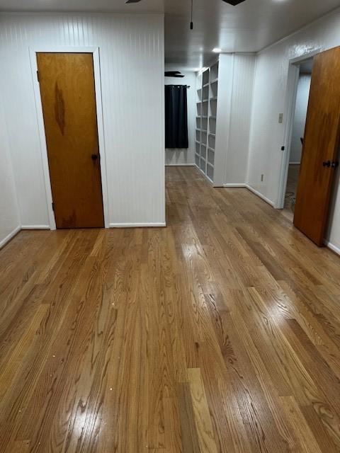 spare room with built in features, ceiling fan, baseboards, and wood finished floors