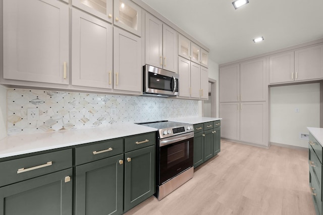 928 College St, Sulphur Springs, TX 75482 - kitchen with backsplash, light countertops, light wood-style floors, green cabinetry, and stainless steel appliances