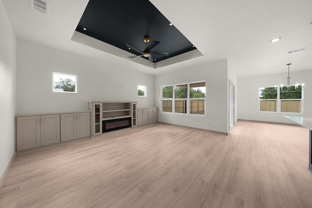 928 College St, Sulphur Springs, TX 75482 - unfurnished living room featuring visible vents, light wood-type flooring, a tray ceiling, ceiling fan with notable chandelier, and a wealth of natural light