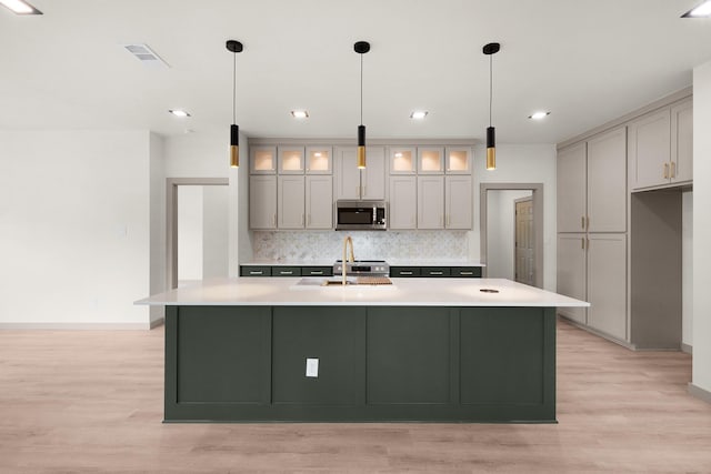 928 College St, Sulphur Springs, TX 75482 - kitchen with decorative backsplash, baseboards, light wood-type flooring, stainless steel microwave, and a sink