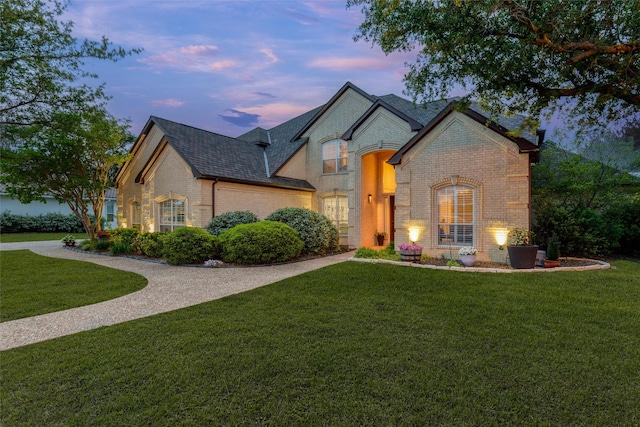 french provincial home featuring brick siding, a shingled roof, and a lawn