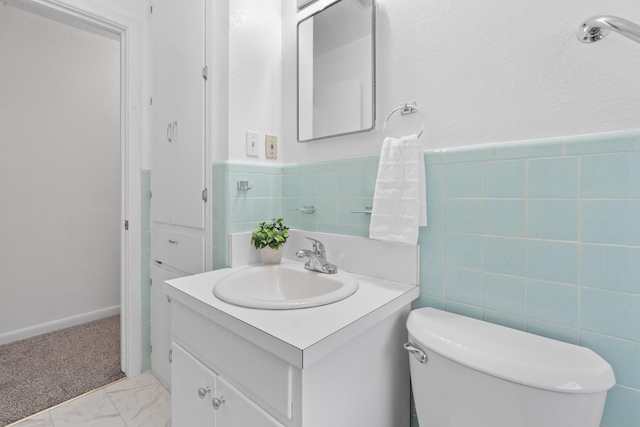half bathroom with vanity, a wainscoted wall, toilet, and tile walls