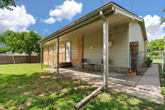 back of property featuring fence, brick siding, a gate, a patio area, and a lawn