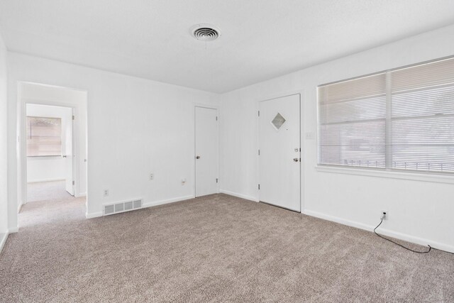 carpeted spare room featuring baseboards, visible vents, and a wealth of natural light