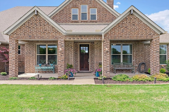 craftsman house featuring a shingled roof, brick siding, a front yard, a chimney, and a patio