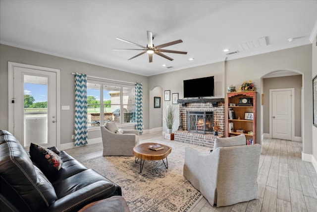 living room featuring crown molding, ceiling fan, a fireplace, arched walkways, and light wood-type flooring