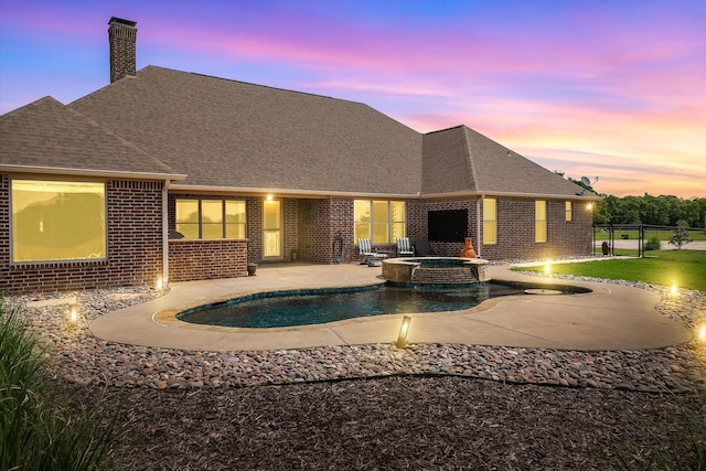 back of property at dusk featuring a chimney, a patio area, brick siding, fence, and a shingled roof