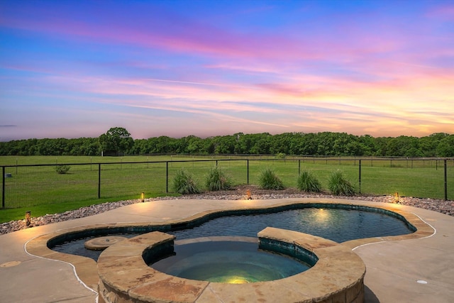 pool at dusk with an in ground hot tub, fence, a fenced in pool, a yard, and a rural view
