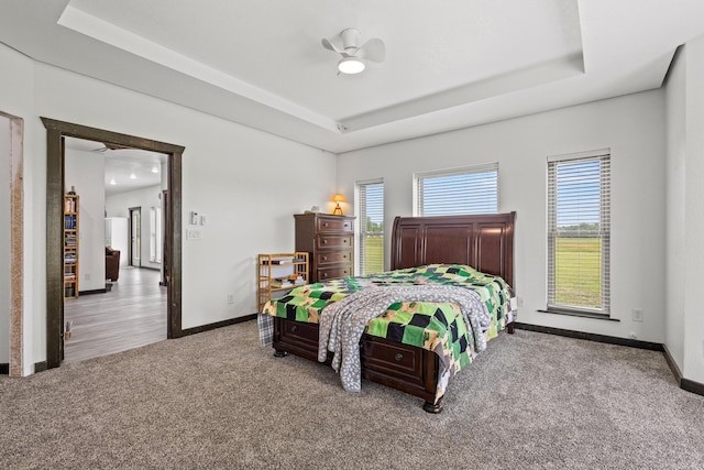 carpeted bedroom with baseboards, a ceiling fan, and a raised ceiling