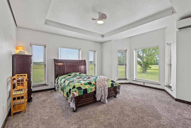 carpeted bedroom with baseboards, ceiling fan, a wall mounted air conditioner, and a raised ceiling