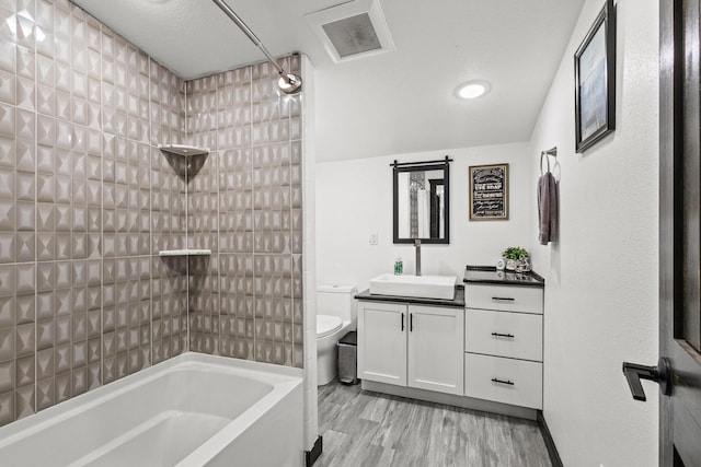 full bath featuring visible vents, vanity, wood finished floors, shower / bathtub combination, and toilet